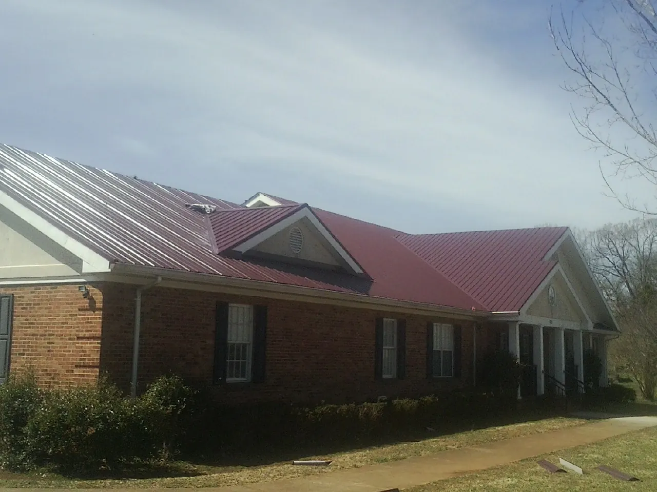 Red metal roof with gabled entries on a long brick building, from a Hail Damage Roof Repair job in Mesa